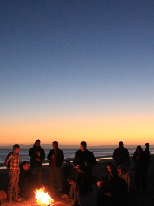 Teammates around a beach bonfire at dusk