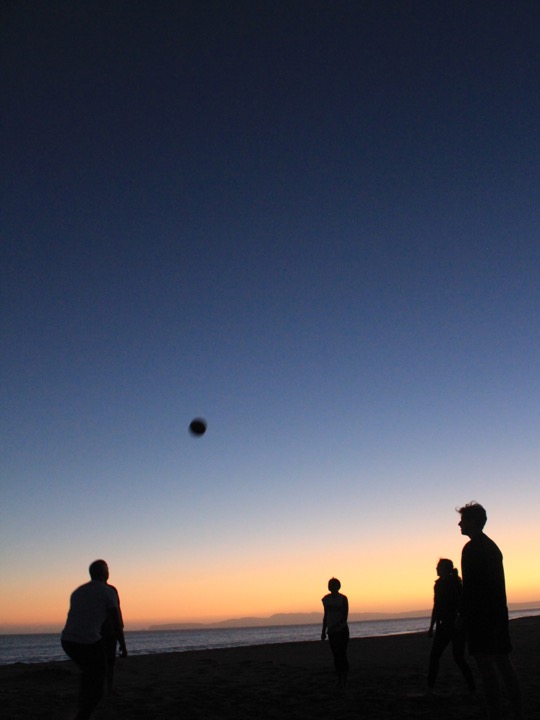 Teammates playing beach volleyball at twilight