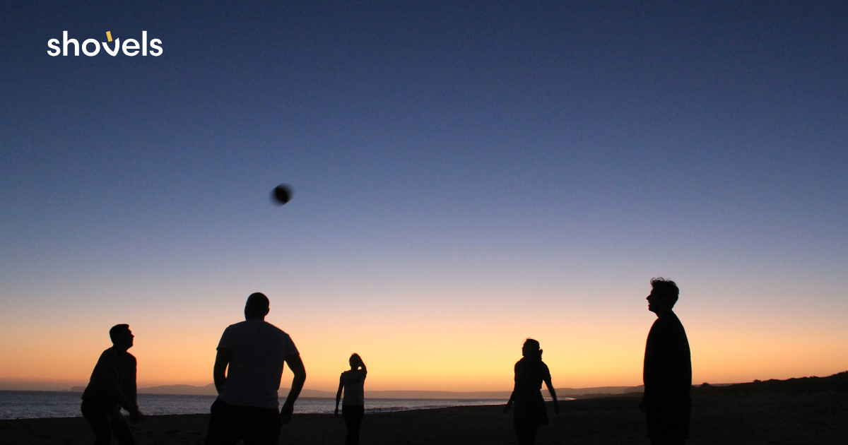 Team members silhouetted against the sunset playing volleyball on the beach